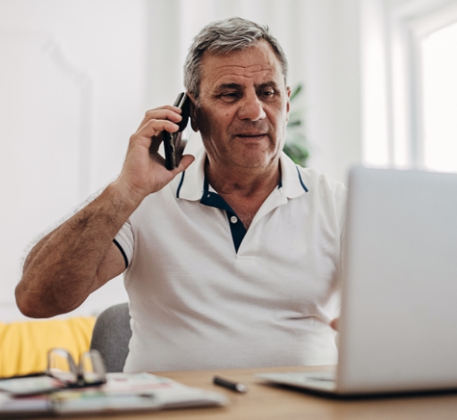 Man talking on phone while looking at laptop.